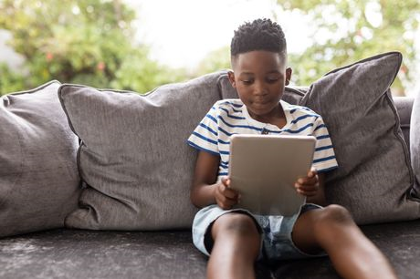 Young boy using a tablet while sitting on the sofa in the living room