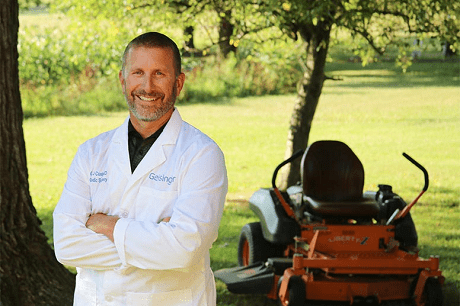 Orthopaedic surgeon Gerard Cush, MD, stands in front of his lawnmower at home.