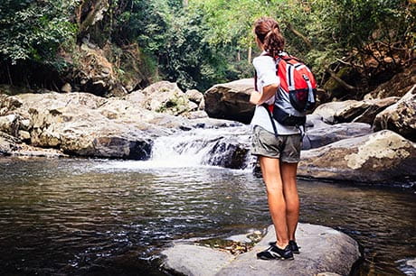 Woman hiking along a local waterway stops to enjoy a small waterfall.