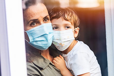 Mother and young son wearing masks as they look out a large window.