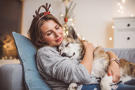 Getting a break from the holidays, a young woman relaxes by holding her dog on the couch.