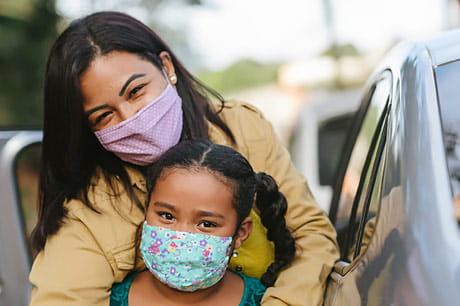 Mother and child wearing a mask in a store parking lot.