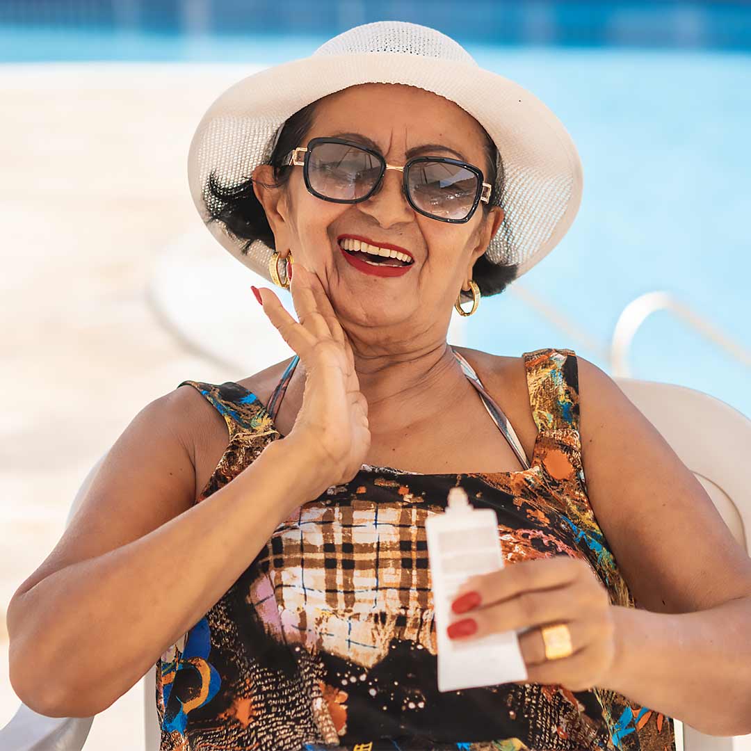 Senior woman applying SPF outdoors to protect from sun damage.