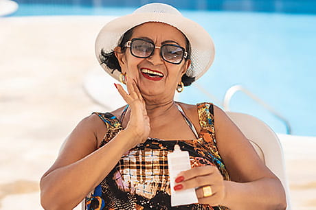 Senior woman applying SPF outdoors to protect from sun damage.