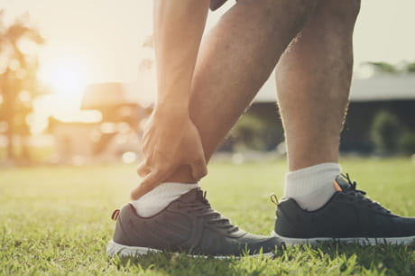 Close up shot of man standing grasping ankle in pain