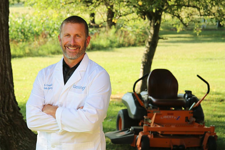 Orthopaedic surgeon Gerard Cush, MD, stands in front of his lawnmower at home. 
