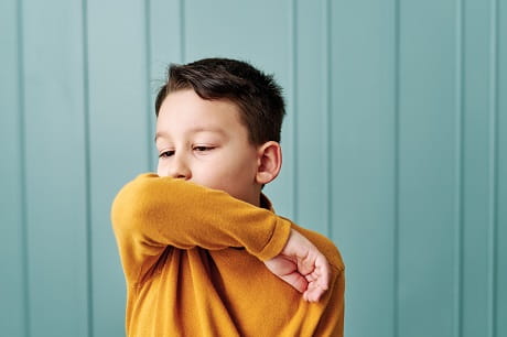 Kid sneezing into his arm