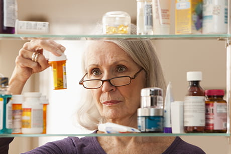 Woman looking at multiple pill bottles at home