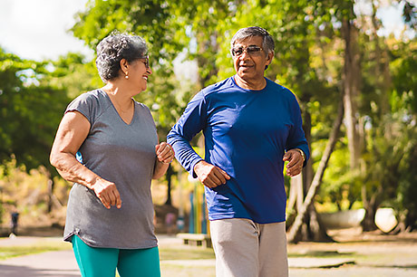 A woman and a man walk briskly through the park.