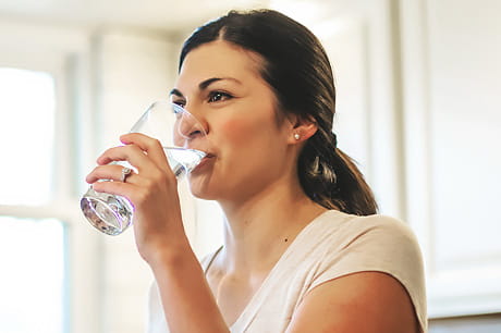 A young woman drinks a glass of water to boost her bladder health.
