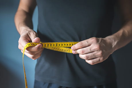 An physically fit adult male measures his waistline.