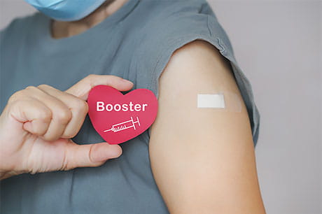 A woman holding a heart-shaped booster icon after receiving a shot.