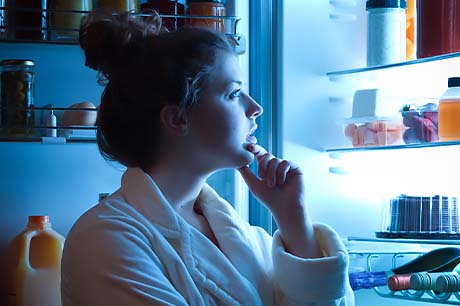 A young woman looks for a healthy late-night snack in the refrigerator.