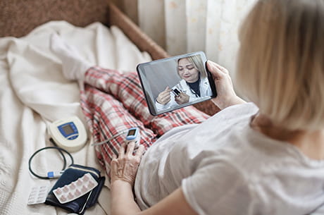 woman in bed talking to her doctor through telemedicine 