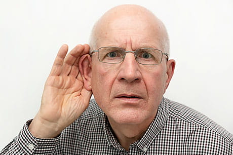 An elderly man struggles to hear conversation.