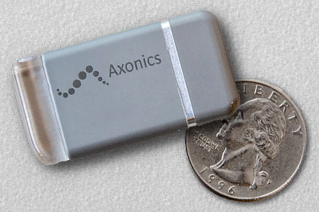 A sacral nerve stimulator is displayed with a quarter to demonstrate the small size of the device.