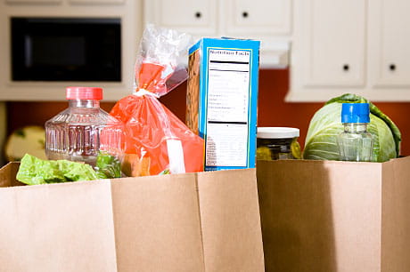 Grocery bags containing assorted items sit on a kitchen counter.