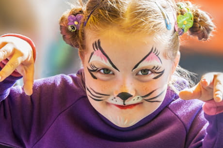 Young girl smiling in cat face paint for Halloween.