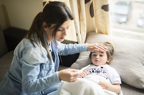 Mother taking her young child's temperature with a thermometer.