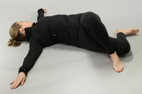 Woman practicing yoga doing a reclining spinal twist pose