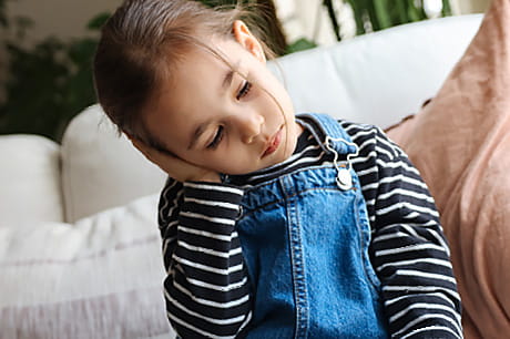 A young girl holds her ear in pain - a sign that she may have an ear infection.