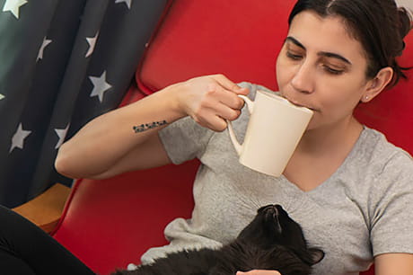 A woman suffering from a sinus infection takes comfort in a warm drink and her cat.