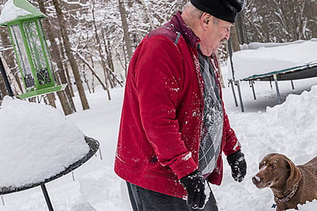 A senior citizen takes his dog outside for some playtime after a recent snowfall.