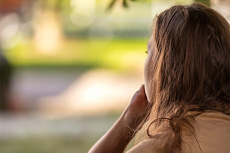 A young female teen sits quietly and contemplatively in a park.