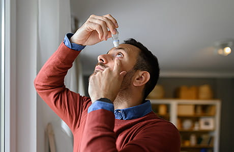 A man adds drop to his eyes to relieve dryness.