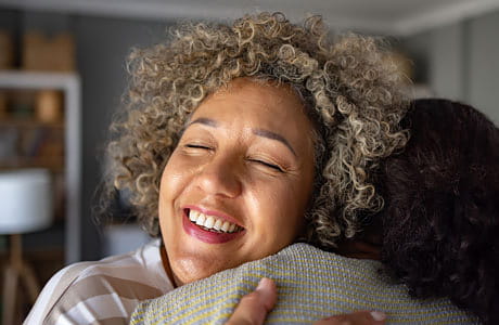 A woman with a warm smile embraces a friend.