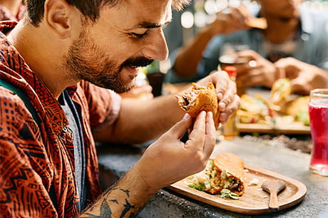 A man enjoys tacos while dining with friends.