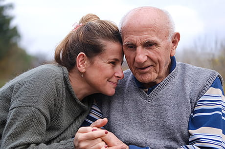 A daughter lovingly embraces the hands of her elderly father.