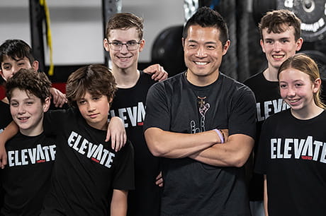 A man stands in the middle of a group of smiling teenagers.