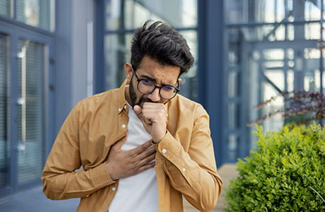 A man stands outside a building coughing