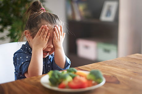 Girl covering her eyes in front of veggie plate