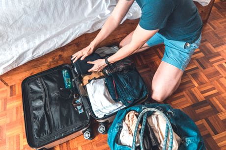 Man packing suitcase and weekend bag with clothing.