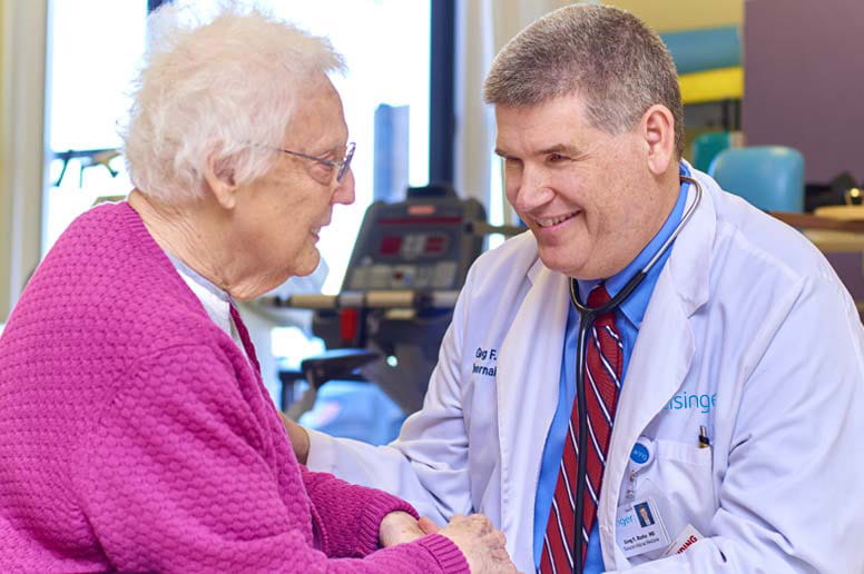 Kneeling doctor talking with seated elderly patient