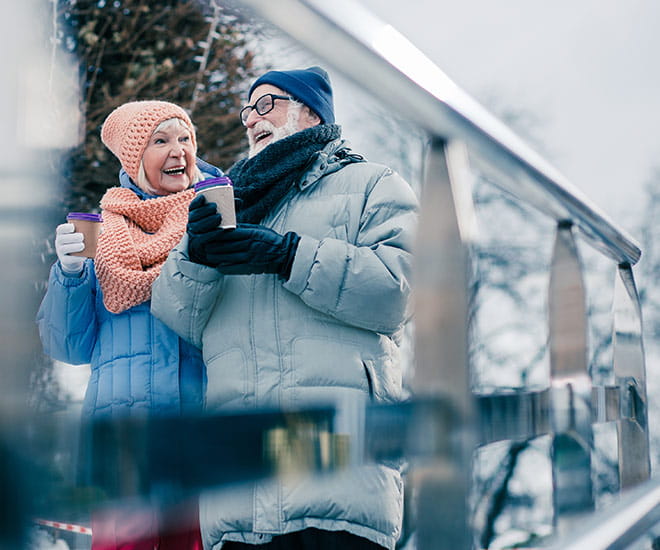 Older male and female couple walking through a park drinking hot chocolate