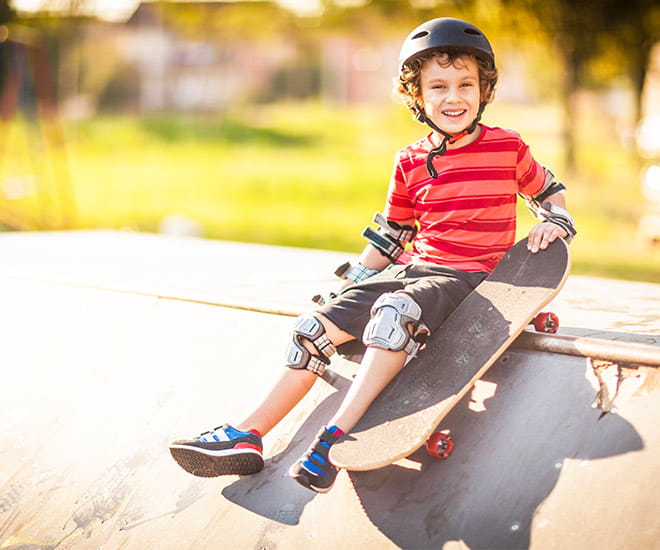 child at skatepark sitting on a ramp with skateboard in hand