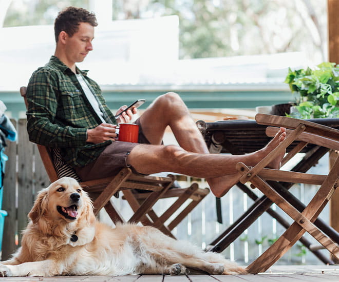 A side view shot of a young man sitting down on a chair outside his house using his smart phone to have a virtual urgent care visit