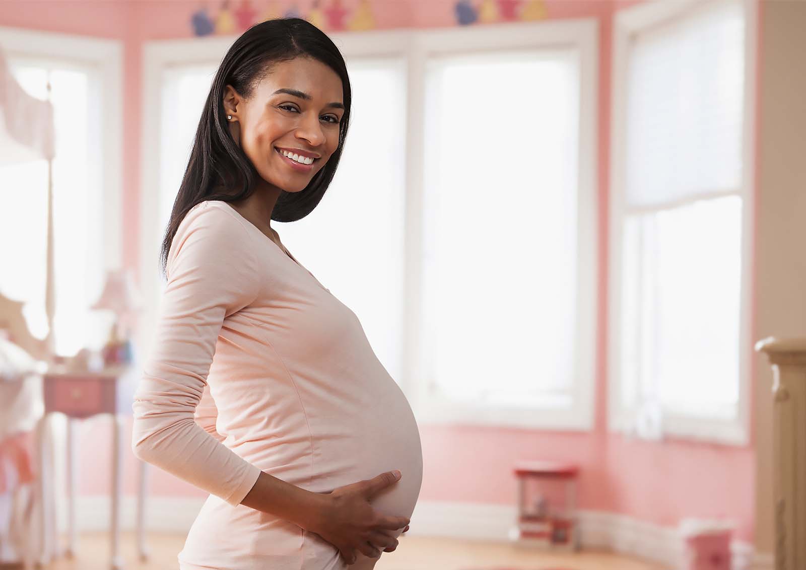 A young pregnant mother poses in her future nursery bedroom.