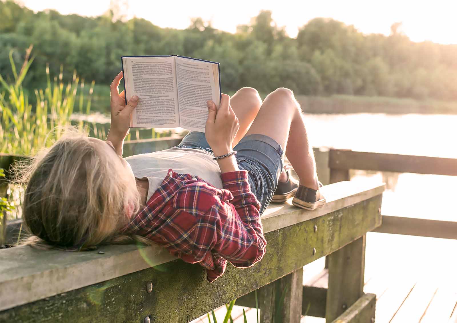 Young male student reading on a dock at sunrise.