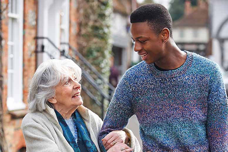 A young man graciously escorts an elderly woman down the street.