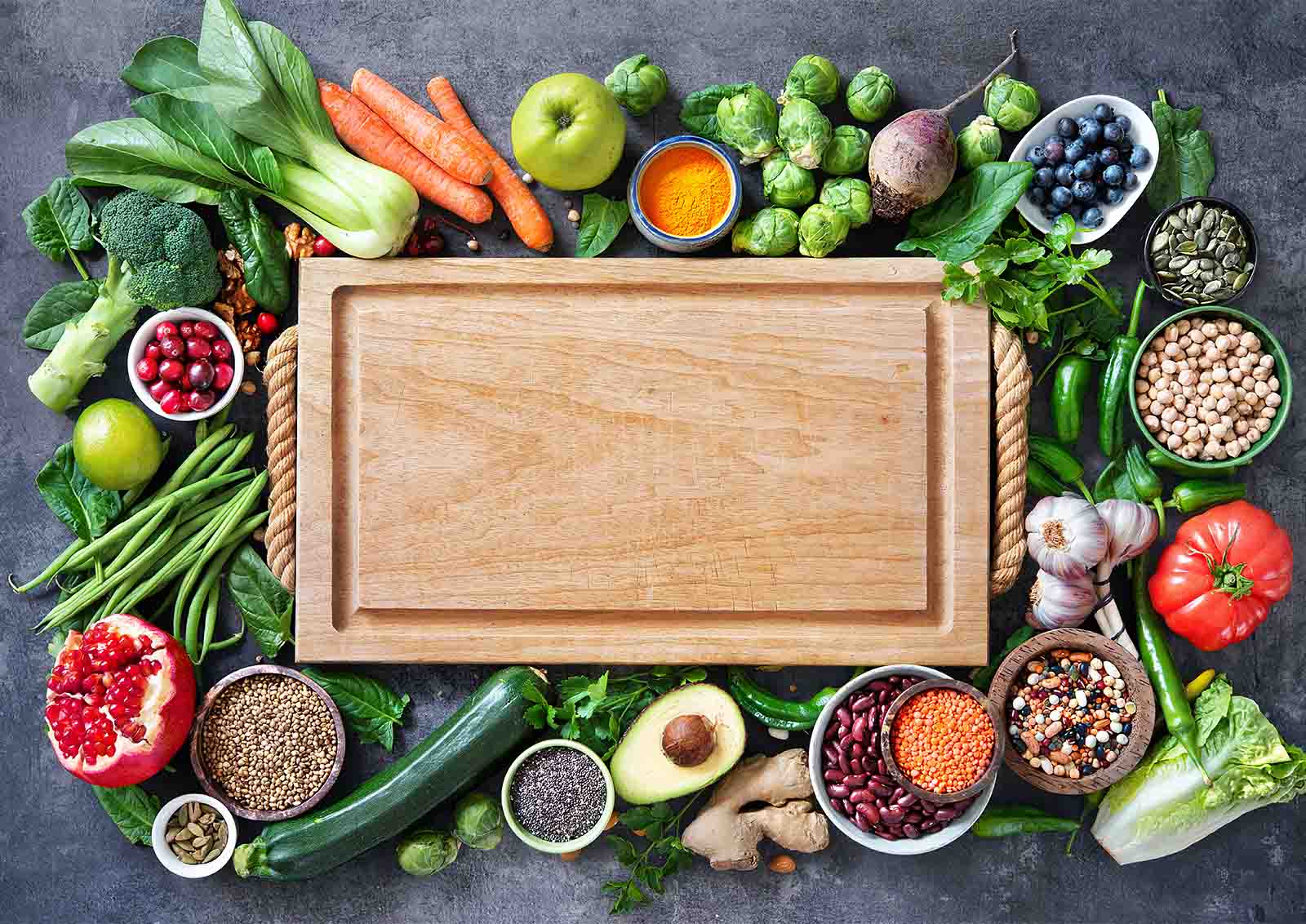 A bounty of fruits, nuts, and vegetables surrounds a large cutting board.