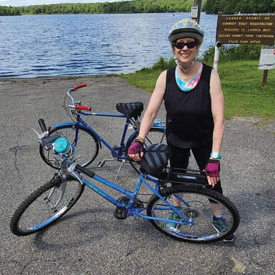 Joanne Bridgman stands with her bicycle with a lake in the background.