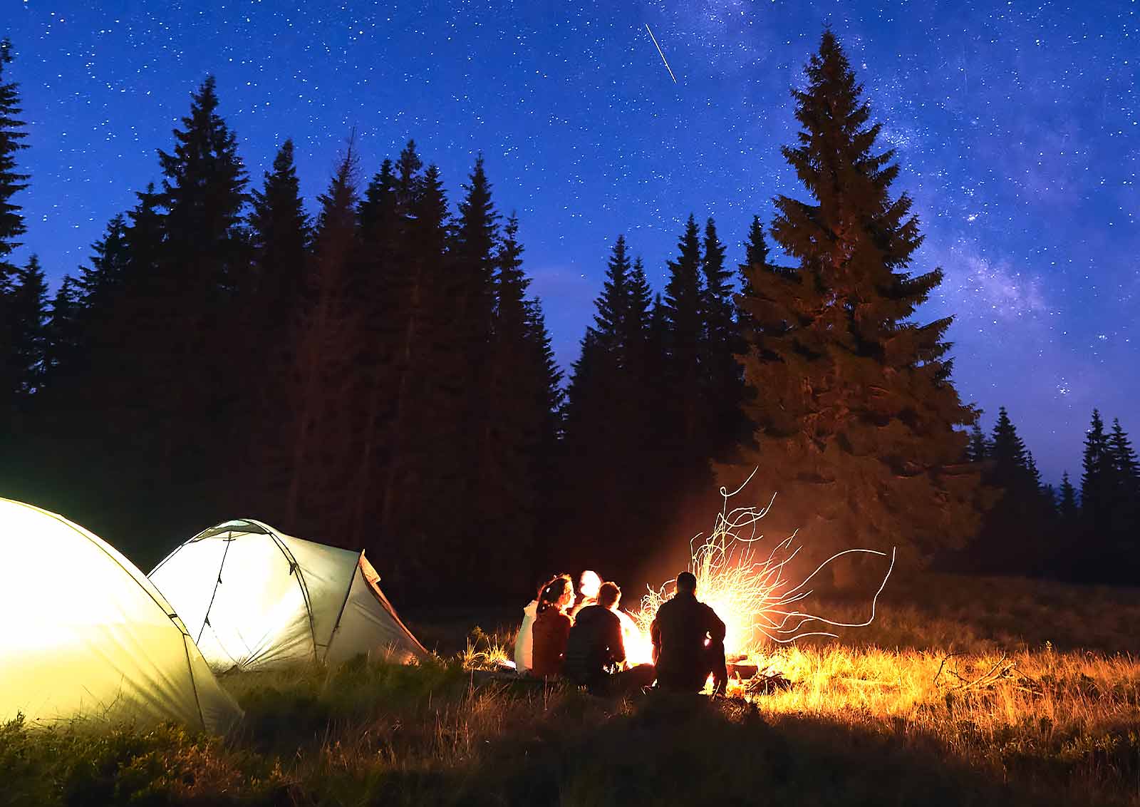 Campers enjoying a fire under the the star-filled nighttime sky.