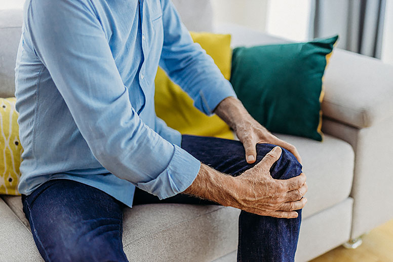 A man is seated on a couch and holds his knee.