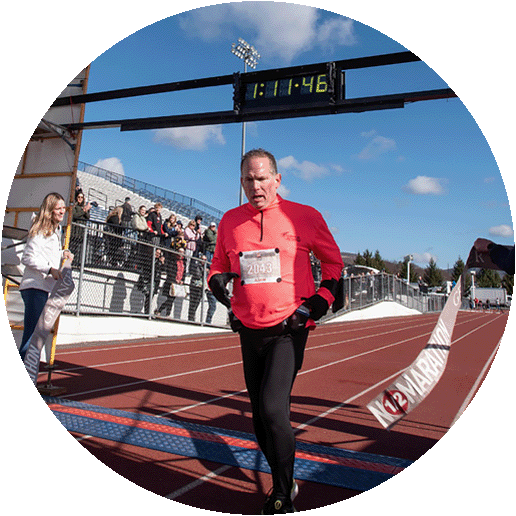 A middle-aged man is running in a road race and crosses the finish line.