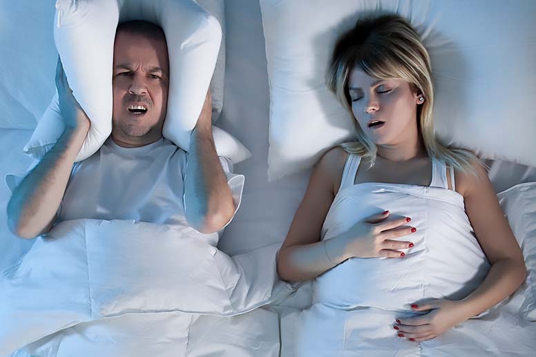 A man struggles to sleep while his wife is snoring next to him in bed.