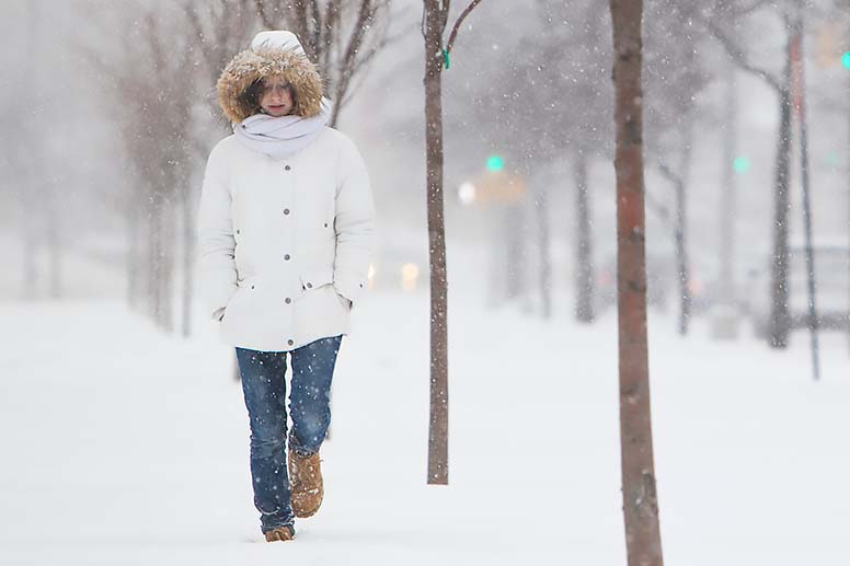 A woman walks alone on a city sidewalk in the snow.
